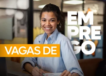 Jovem mulher negra sorridente com cabelos cacheados presos, vestindo camisa social azul claro, sentada em um escritório. Sobre a imagem, há o texto em destaque "VAGAS DE EMPREGO" em cores branco e laranja.