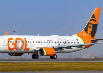Aeronave Boeing 737 da GOL Linhas Aéreas taxiando em uma pista de aeroporto sob o sol. O avião possui a fuselagem branca com o logotipo laranja e uma pintura especial na cauda celebrando 150 anos com a imagem de Santos Dumont.