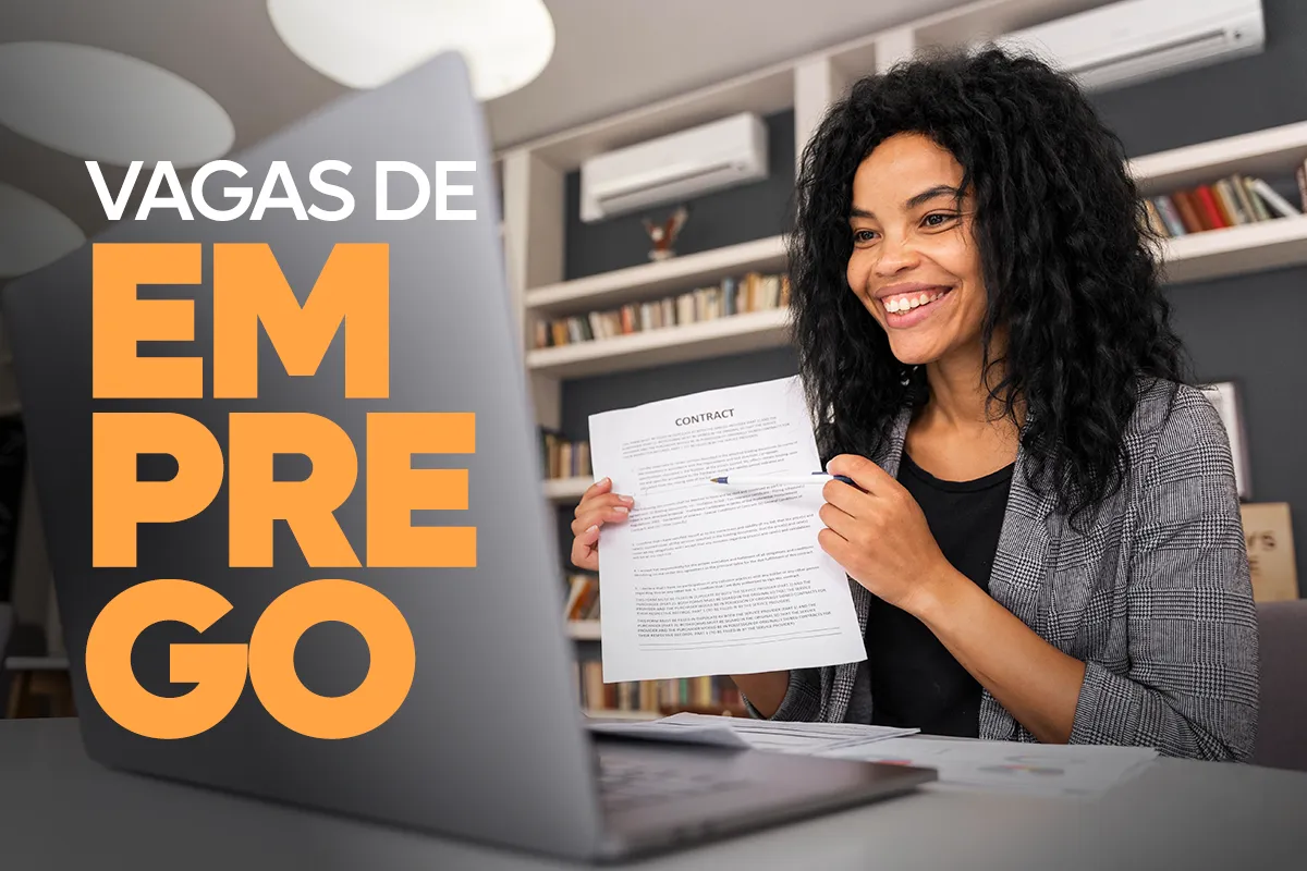 Mulher negra sorridente com cabelos cacheados, vestindo blazer cinza, segurando um documento de contrato em frente a um notebook. Ao lado esquerdo, o texto gráfico em destaque diz "VAGAS DE EMPREGO" em letras grandes brancas e laranjas.