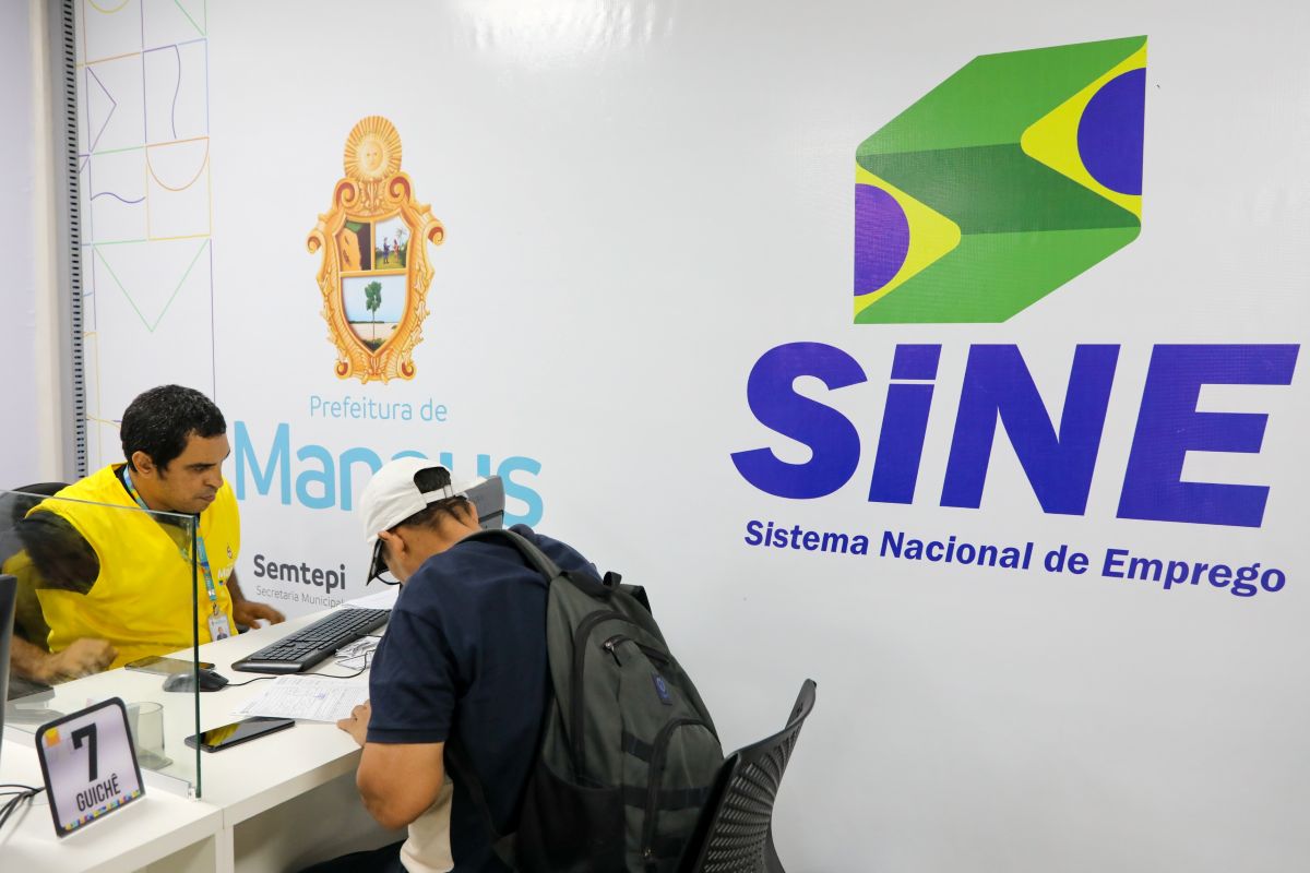 Atendente e candidato em guichê do Sine Manaus com logo do Sistema Nacional de Emprego ao fundo