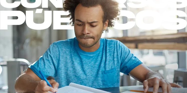 Homem jovem de cabelo afro e camiseta azul estudando concentrado com cadernos e canetas, com a sobreposição de texto "Concursos Públicos".