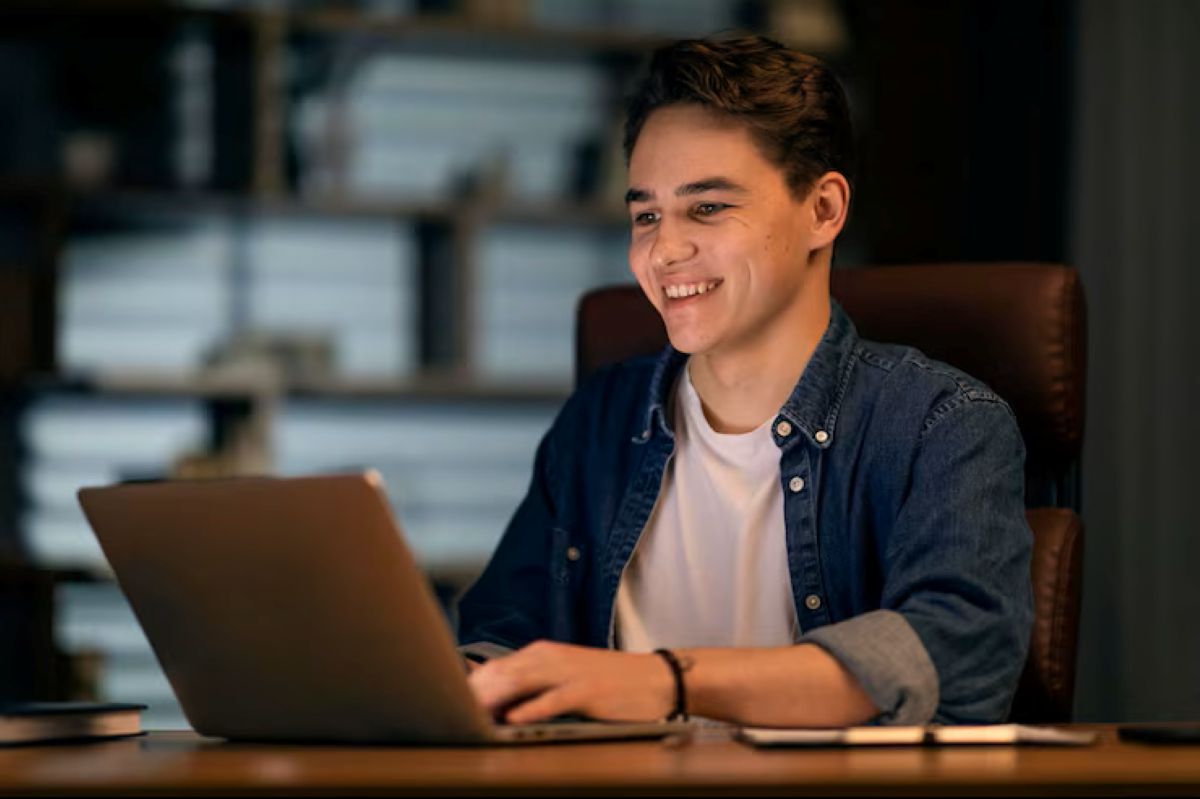 Jovem sorrindo em frente ao notebook em um escritório escuro