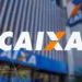 Logotipo da CAIXA em letras brancas com o "X" laranja, em destaque sobre a fachada de um prédio moderno de vidro e metal, representando uma das agências do banco.