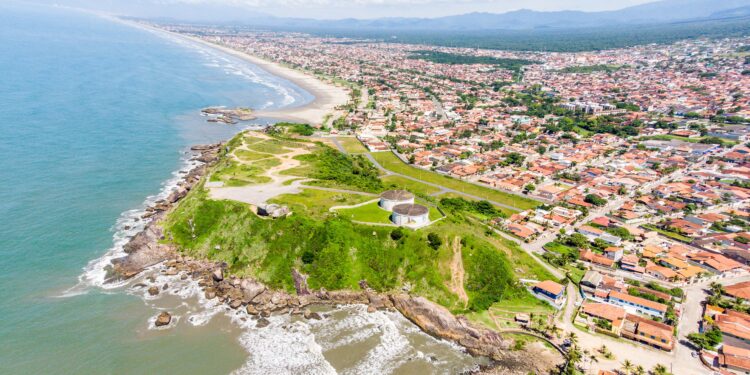 Vista aérea mostra praia extensa, morros verdes e bairros residenciais da cidade litorânea