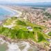 Vista aérea mostra praia extensa, morros verdes e bairros residenciais da cidade litorânea
