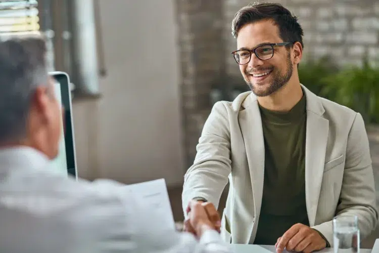 Homem sorrindo aperta a mão de outro durante entrevista de emprego