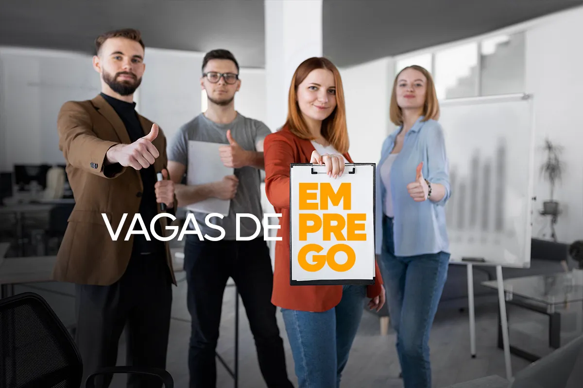 Grupo de quatro jovens profissionais em um escritório, sorrindo e fazendo sinal de positivo com o polegar, enquanto a mulher à frente segura uma prancheta com o texto "VAGAS DE EMPREGO".