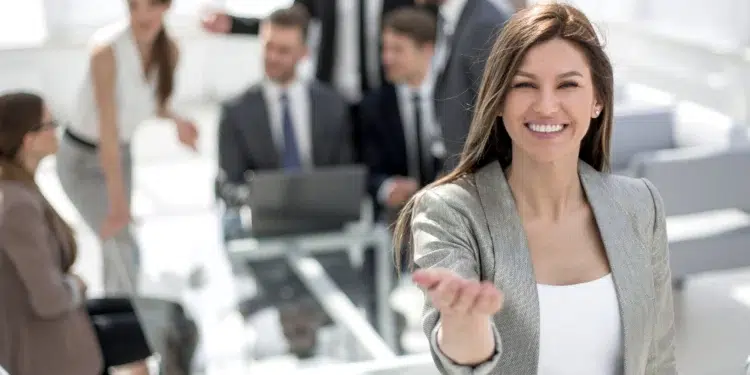 Mulher sorrindo e acenando em sala de reunião com equipe ao fundo