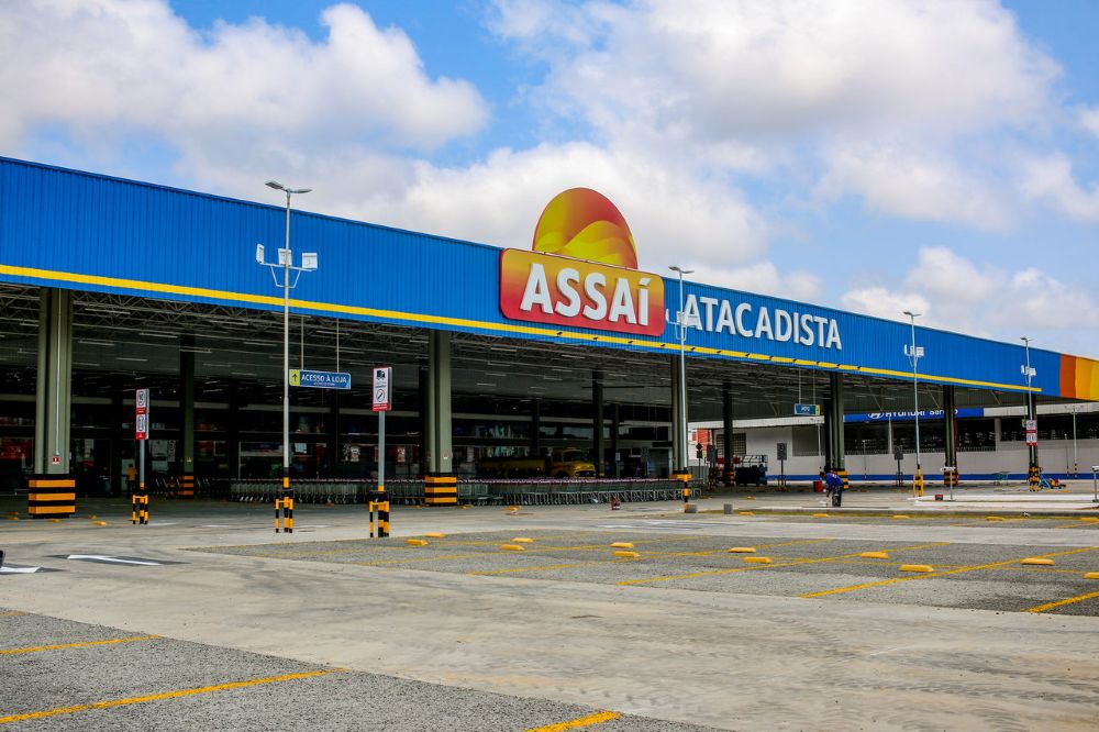 Fachada externa de uma loja Assaí Atacadista iluminada à noite, mostrando o letreiro principal e o estacionamento movimentado.