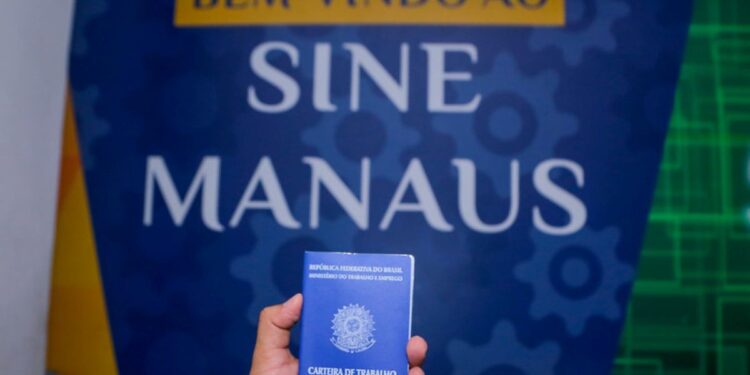 Mão segurando carteira de trabalho em frente ao banner do Sine Manaus