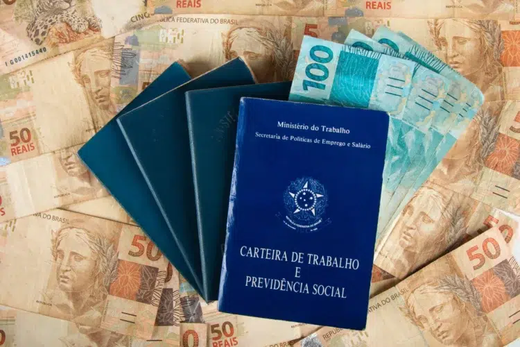 Carteiras de trabalho ao lado de notas de reais simbolizando vagas de emprego