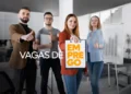 Quatro profissionais em escritório, mulher ruiva segura prancheta com texto "Vagas de Emprego" em laranja