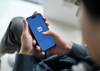 Pessoa segurando um smartphone com o logotipo do LinkedIn aberto na tela, em um ambiente de escritório.