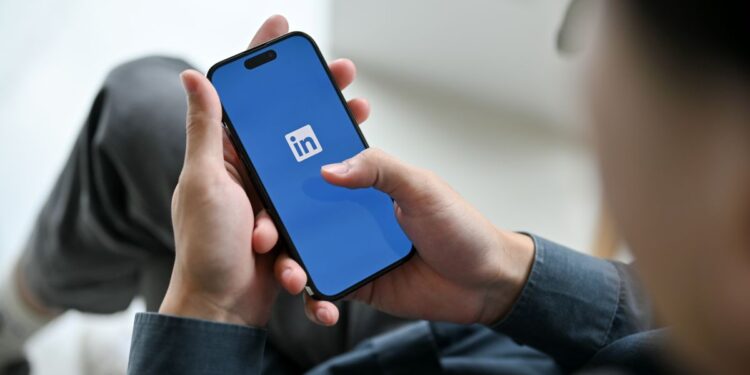 Pessoa segurando um smartphone com o logotipo do LinkedIn aberto na tela, em um ambiente de escritório.