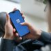 Pessoa segurando um smartphone com o logotipo do LinkedIn aberto na tela, em um ambiente de escritório.
