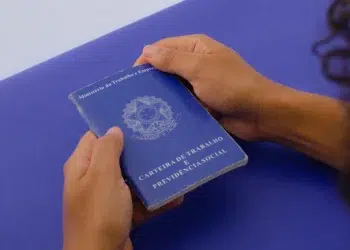 Pessoa segura uma carteira de trabalho azul com ambas as mãos sobre superfície azul