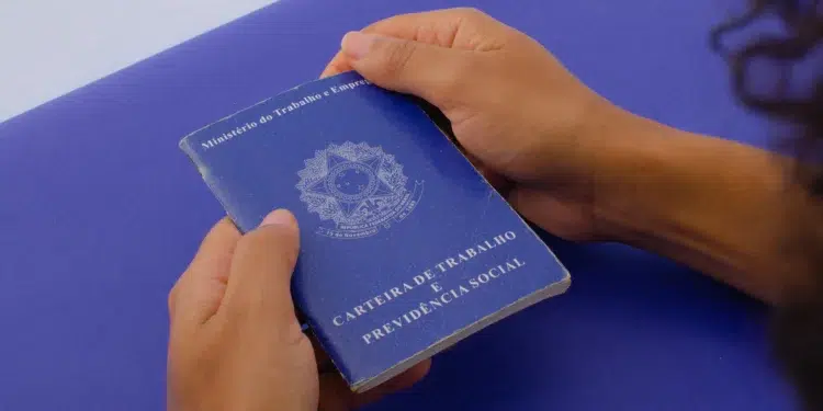 Pessoa segura uma carteira de trabalho azul com ambas as mãos sobre superfície azul