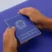 Pessoa segura uma carteira de trabalho azul com ambas as mãos sobre superfície azul