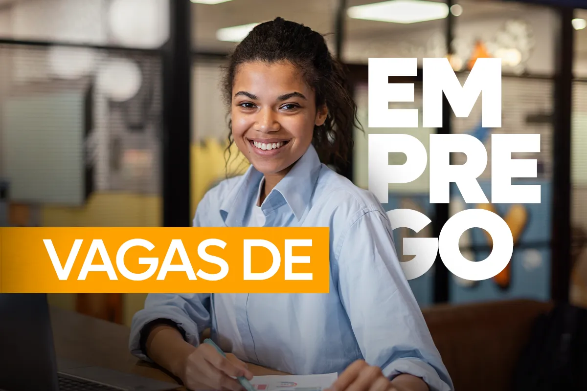 Mulher jovem sorridente sentada à mesa com papéis, ao fundo um ambiente de escritório, com o texto "Vagas de Emprego" em destaque branco e amarelo.