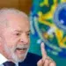 Presidente Lula gesticula com dedo indicador erguido durante entrevista no Palácio do Planalto, com bandeira do Brasil ao fundo.