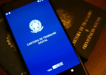 Smartphone exibindo o aplicativo da Carteira de Trabalho Digital sobre uma Carteira de Trabalho física de papel.