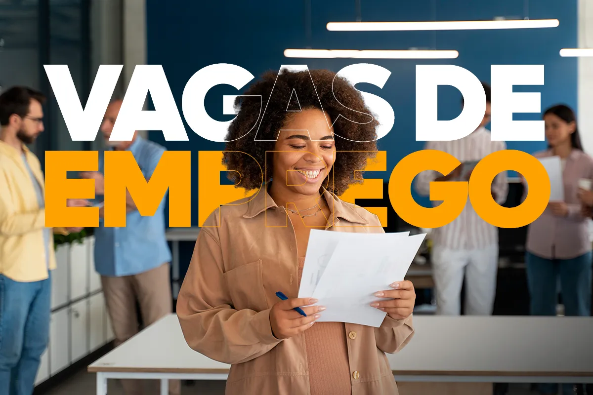 Mulher negra sorridente segurando currículos em papel em um escritório. Ao fundo, outras pessoas desfocadas trabalham. Sobreposta à imagem, há a escrita estilizada "VAGAS DE EMPREGO".